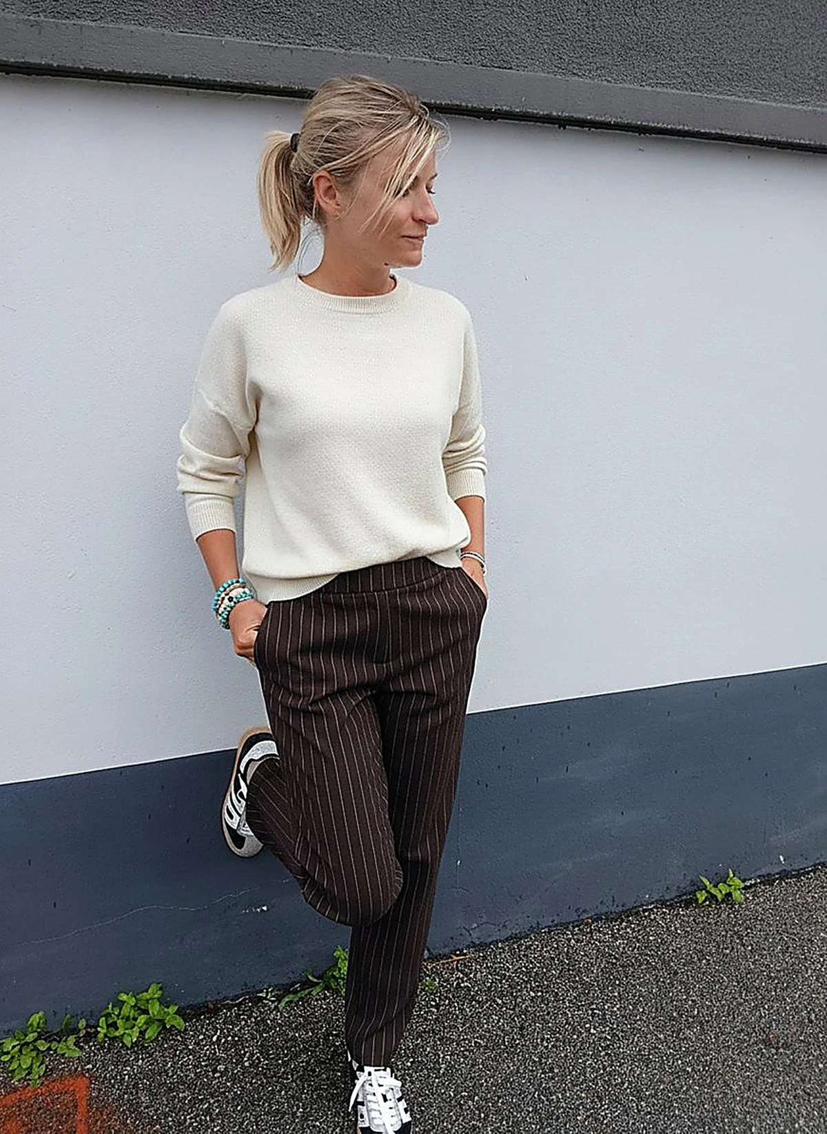 Laurie en pantalon Colette fines rayures espresso, adossée au mur de la boutique