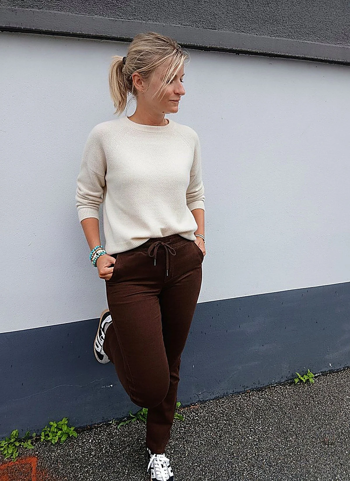 Laurie en pantalon Stella velours, adossée au mur de la boutique