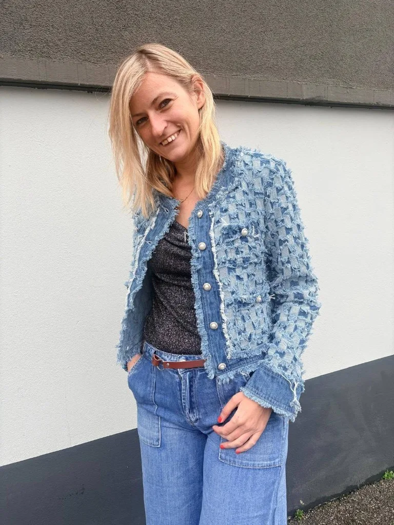 Veste en denim clair aux bords effilochés, boutons nacrés, portée sur un top sombre